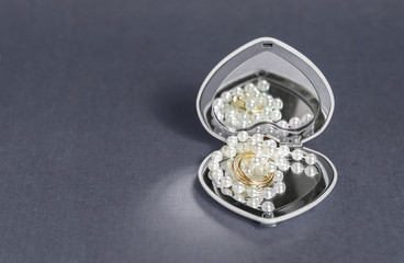 Wedding rings with gift decoration pearl and heart shaped mirror box on gray background