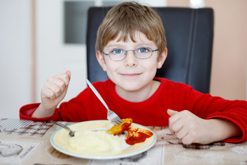 Adorable little school boy eating potato mash and chicken breast indoor