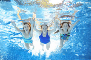 Family swims in pool under water, happy active mother and children have fun, fitness and sport with kids on summer vacation
