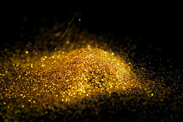 Fototapeta na wymiar Sprinkle glitter gold dust on a black background with copy space