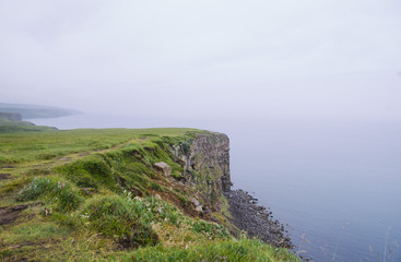 rock beach cliff edge on a foggy rainy weather, dark ocean 