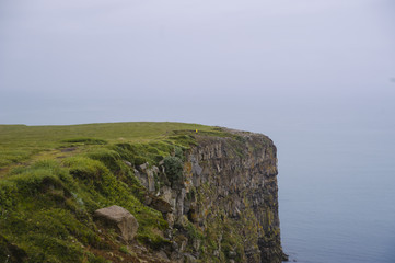 rock beach cliff edge on a foggy rainy weather, dark ocean 