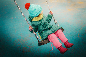 little girl swinging on a swing at the playground in autumn