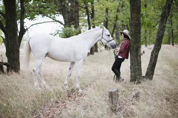 happy girl standing with her horse grazing nearby in the forest