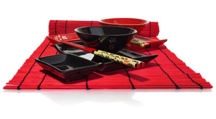 Red and black set of dishes for sushi on the red wooden mat.