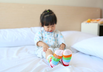 Lovely little asian girl trying to put a socks on the bed.