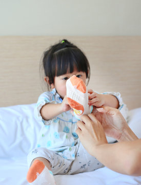 Mother Trying To Put A Socks For Her Daughter On The Bed.