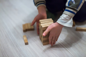 A child dressed not neatly in a home clothes playing on the floor. Man builds a tower of wooden bars.