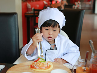 Kid girl in a suit of the little chef make mini pizza, Cooking child concept.