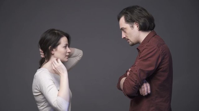 Young couple negotiating, talking to each other, pointing the finger and gesticulating, they have a quarrel, gray background