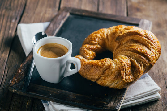Espresso coffee cup and croissant on blank blackboard over wooden table