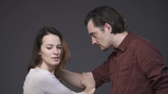Violence in the family. A man aggressively keeping woman's shoulder, a woman is protecting herself, gray background