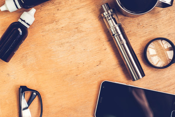 Vaping set, smartphone and coffee on the wood table. Hipster or bussinesman style. Trendy objects with copy space on the wooden background