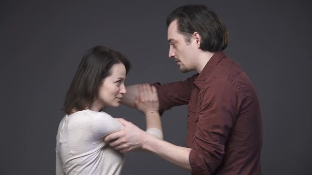 Young couple having a quarrel, woman is crying, a man grabbing her hair, gray background