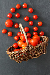 scattered ripe cherry tomatoes in a wicker basket on a black background