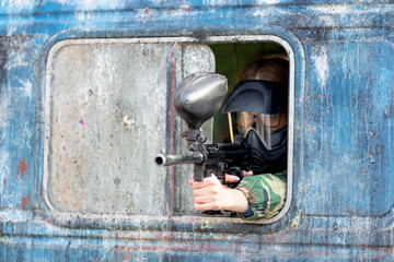 girl playing paintball in overalls with a gun.