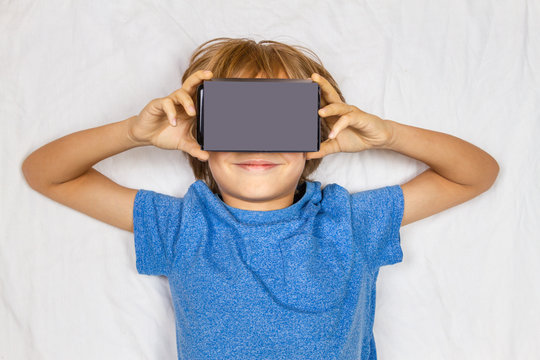 Child liying in white bed with 3D Virtual Reality, VR cardboard glasses