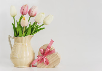 holiday and spring concept/bouquet of wihte and pink tulips and heart shape gift box with pink bow on a white background with space for text