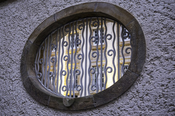 Blick durch ein rundes mit verziertem Metallgitter beschlagenen Fenster auf eine gelbe Häuserfassade