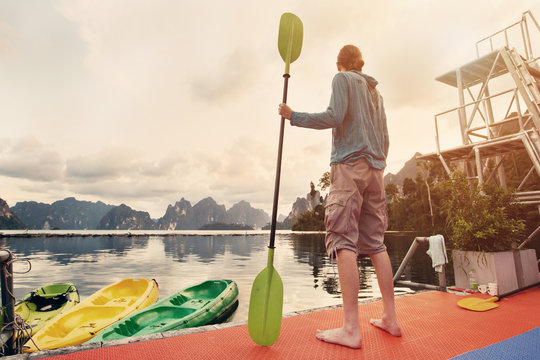 Man holding paddle standing on mountain tropical lake shore. Traveling in Thailand, Cheow Lan Lake, Khao Sok