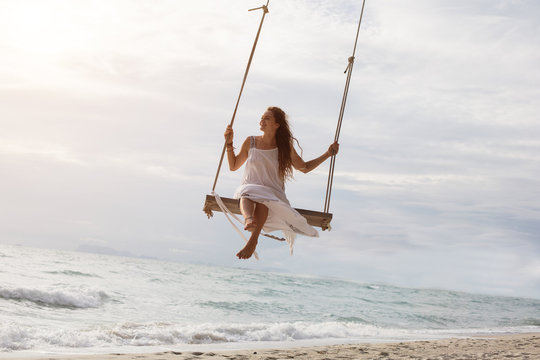 Beautiful young female sitting on the swing on sea shore enjoy summer