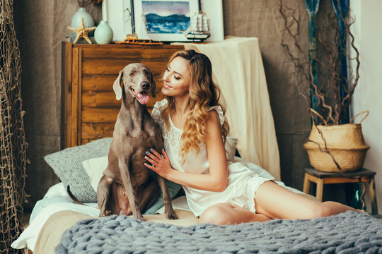 Young And Pretty Woman Playing With Her Dog In Bedroom