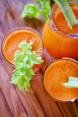 Fresh carrot juice poured into glasses and green celery