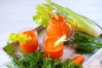 Fresh carrot juice poured into glasses and green celery