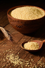 millet in a wooden bowl on a wooden background near the ears of wheat. wooden spoon with millet