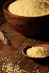 millet in a wooden bowl on a wooden background near the ears of wheat. wooden spoon with millet
