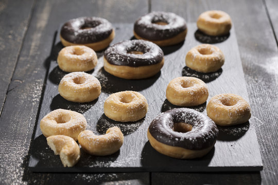 große Donuts mit Schokoladenglasur und kleine Donuts mit Zucker auf schwarzen Holztisch
