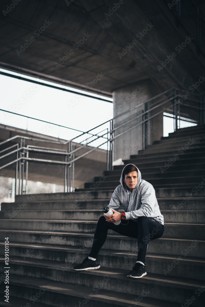 Wall mural Young sportsman sitting at the stairs and resting 