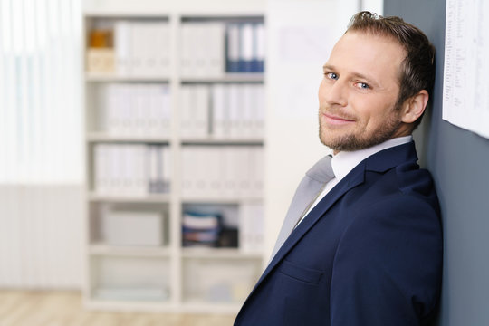 geschäftsmann im büro lehnt sich lässig an die wand