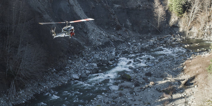 A helicopter flying above a rocky river bed in a valley.