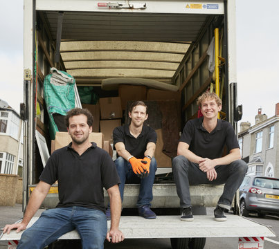 Removals business. Three men in black shirts, sitting having a break at the back of their removals van. 