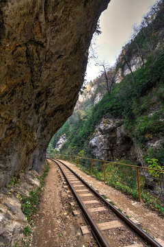Beautiful scenic landscape of narrow-gauge railroad track passing through Guam mountain river canyon in Caucasus mountains at summer. Vertical view