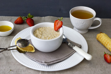 Oatmeal with fresh strawberries on linen fabric. Wafer with a boiled condensed milk and honey for tea. A healthy, delicious breakfast