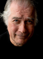  close up portrait headshot of a senior man in his 50's. male wearing black t-shirt and isolated oin black background.