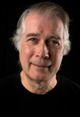  close up portrait headshot of a senior man in his 50's. male wearing black t-shirt and isolated oin black background.