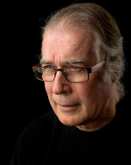  close up portrait headshot of a senior man in his 50's. male wearing black t-shirt and isolated oin black background.