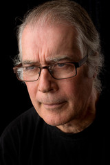  close up portrait headshot of a senior man in his 50's. male wearing black t-shirt and isolated oin black background.