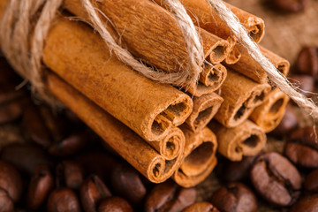 Obraz na płótnie Canvas Coffee beans and cinnamon on a background of burlap. Roasted coffee beans background close up. Coffee beans pile from top with copy space for text. Seasoning. Spice. Cinnamon. Badian. Coffee house.