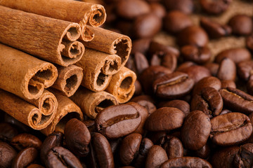 Coffee beans and cinnamon on a background of burlap. Roasted coffee beans background close up. Coffee beans pile from top with copy space for text. Seasoning. Spice. Cinnamon. Badian. Coffee house.