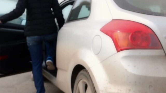 Girl opening car door and sitting in the silver land vehicle out of focus. 