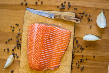 Orange raw fillet of salmon on wooden table with knife and papper