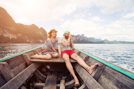 Funny couple: man with a beard and woman wearing hat traveling by boat on tropical mountain lake. Summer travel, family vacation