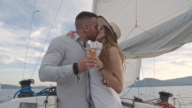 Couple in love drinking champagne from flutes, embracing and tenderly kissing on drifting yacht in slow motion