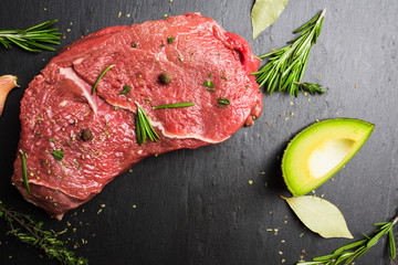 Fresh raw beef meat with avocado and herbs on the black stone background