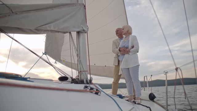 Couple of active seniors standing on yacht, embracing and smiling while cruising on lake
