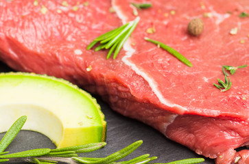 Fresh raw beef meat with avocado and herbs on the black stone background